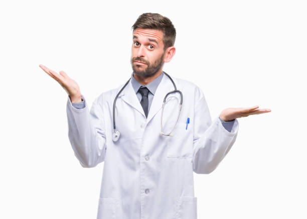 Young handsome doctor man over isolated background clueless and confused expression with arms and hands raised. Doubt concept.